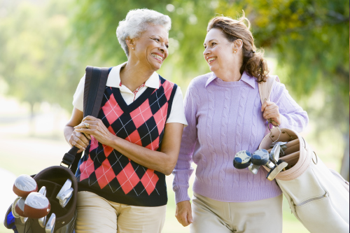 Two women walking and carrying golf clubs